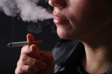 Photo of Woman smoking cigarette on black background, closeup