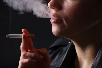 Photo of Woman smoking cigarette on black background, closeup