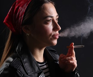 Photo of Woman in bandana smoking cigarette on black background, closeup