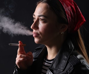 Photo of Woman in bandana smoking cigarette on black background, closeup