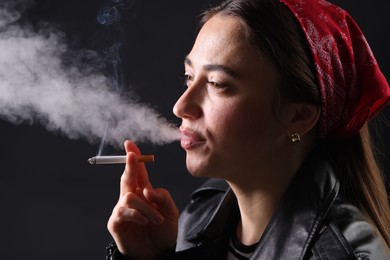 Photo of Woman in bandana smoking cigarette on black background, closeup