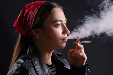 Photo of Woman in bandana smoking cigarette on black background, closeup