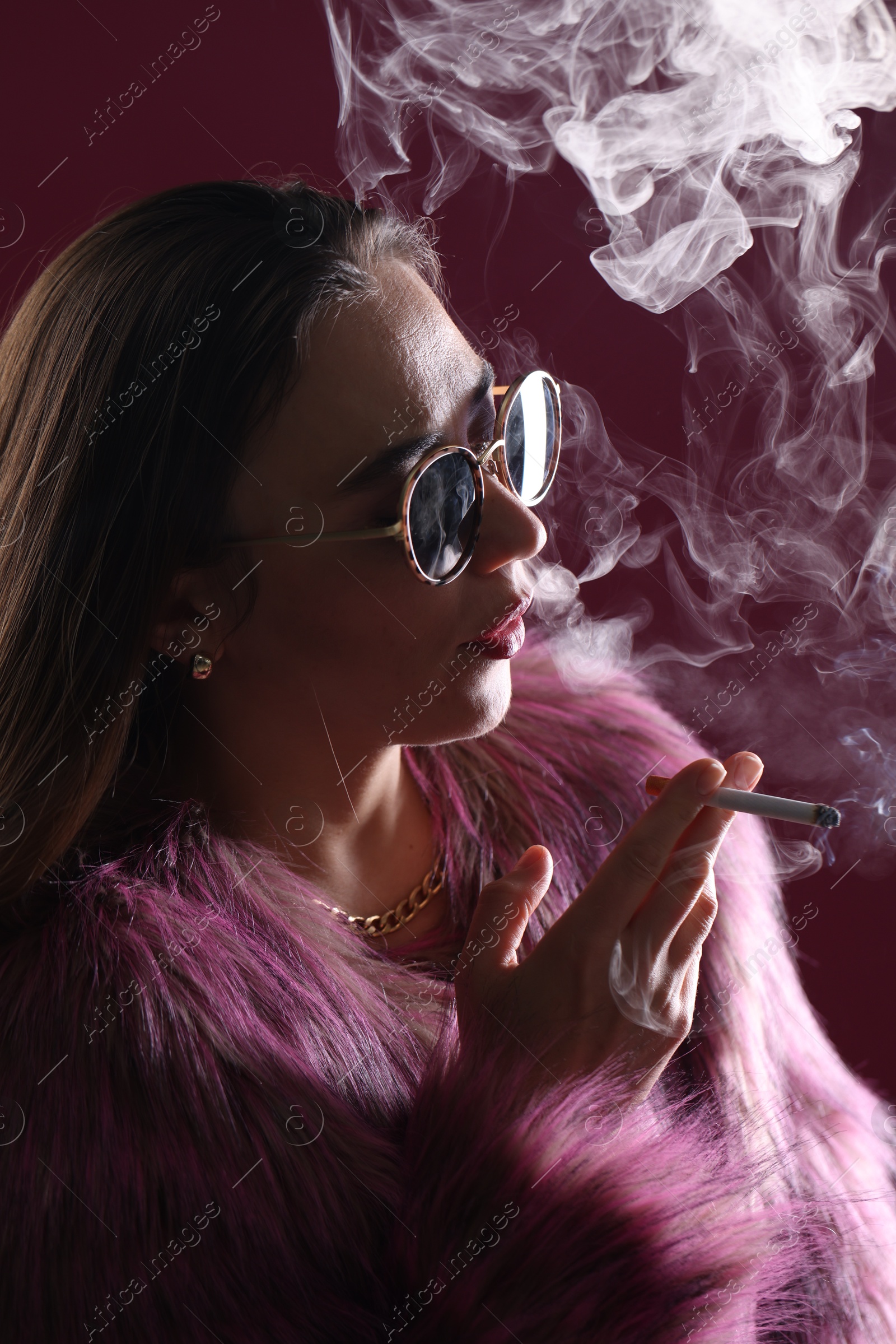 Beautiful woman in fur coat smoking cigarette on dark pink background, closeup Photo of Beautiful woman in fur coat smoking cigarette on dark pink background, closeup