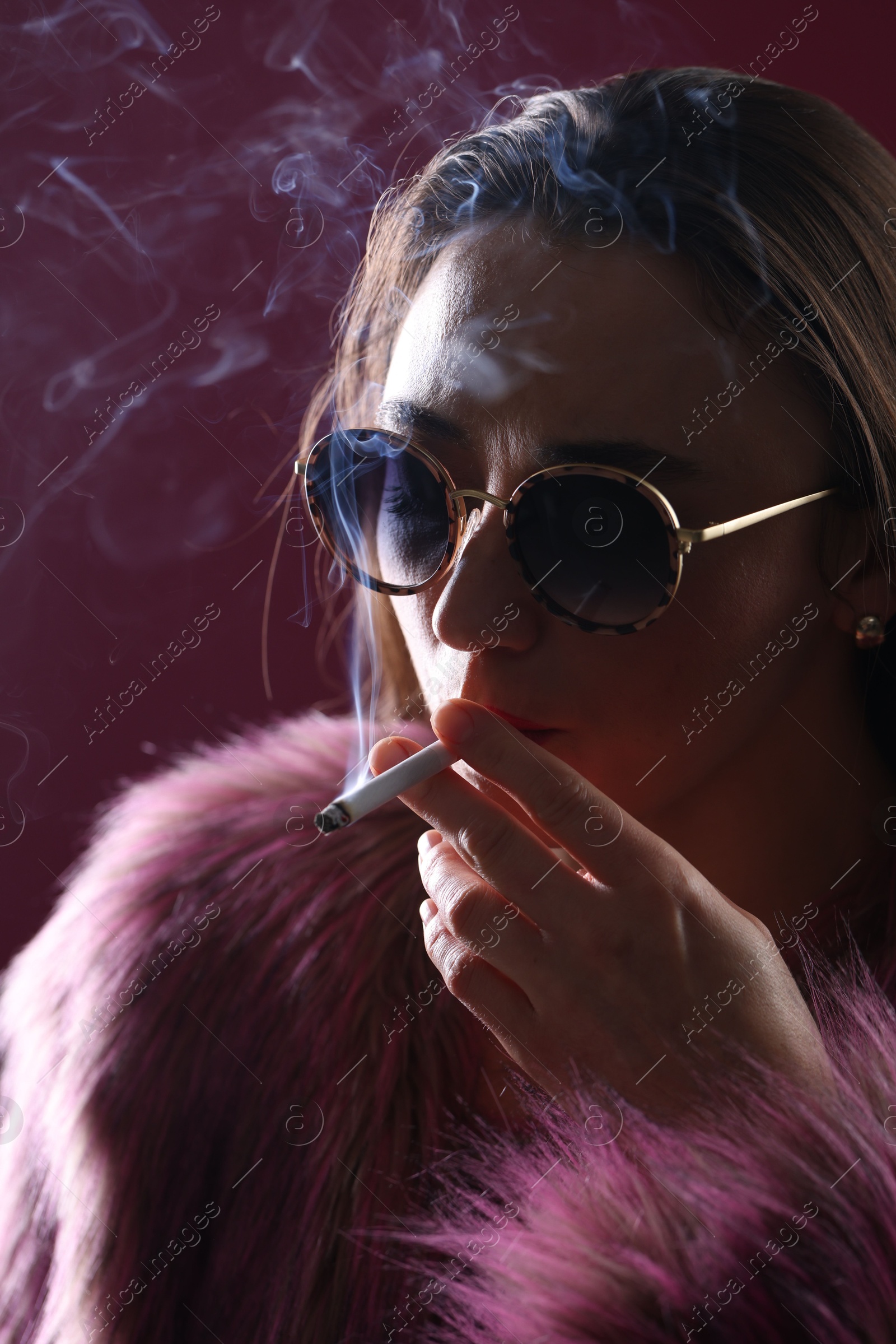 Beautiful woman in fur coat smoking cigarette on dark pink background, closeup Photo of Beautiful woman in fur coat smoking cigarette on dark pink background, closeup