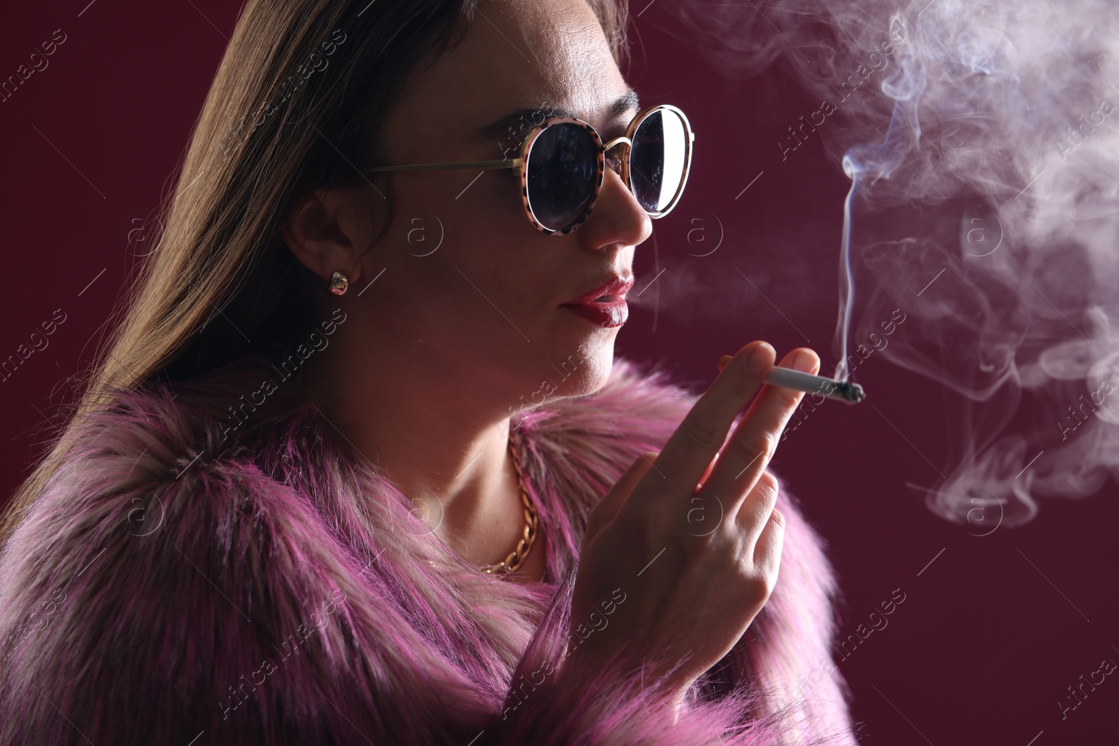 Beautiful woman in fur coat smoking cigarette on dark pink background, closeup Photo of Beautiful woman in fur coat smoking cigarette on dark pink background, closeup