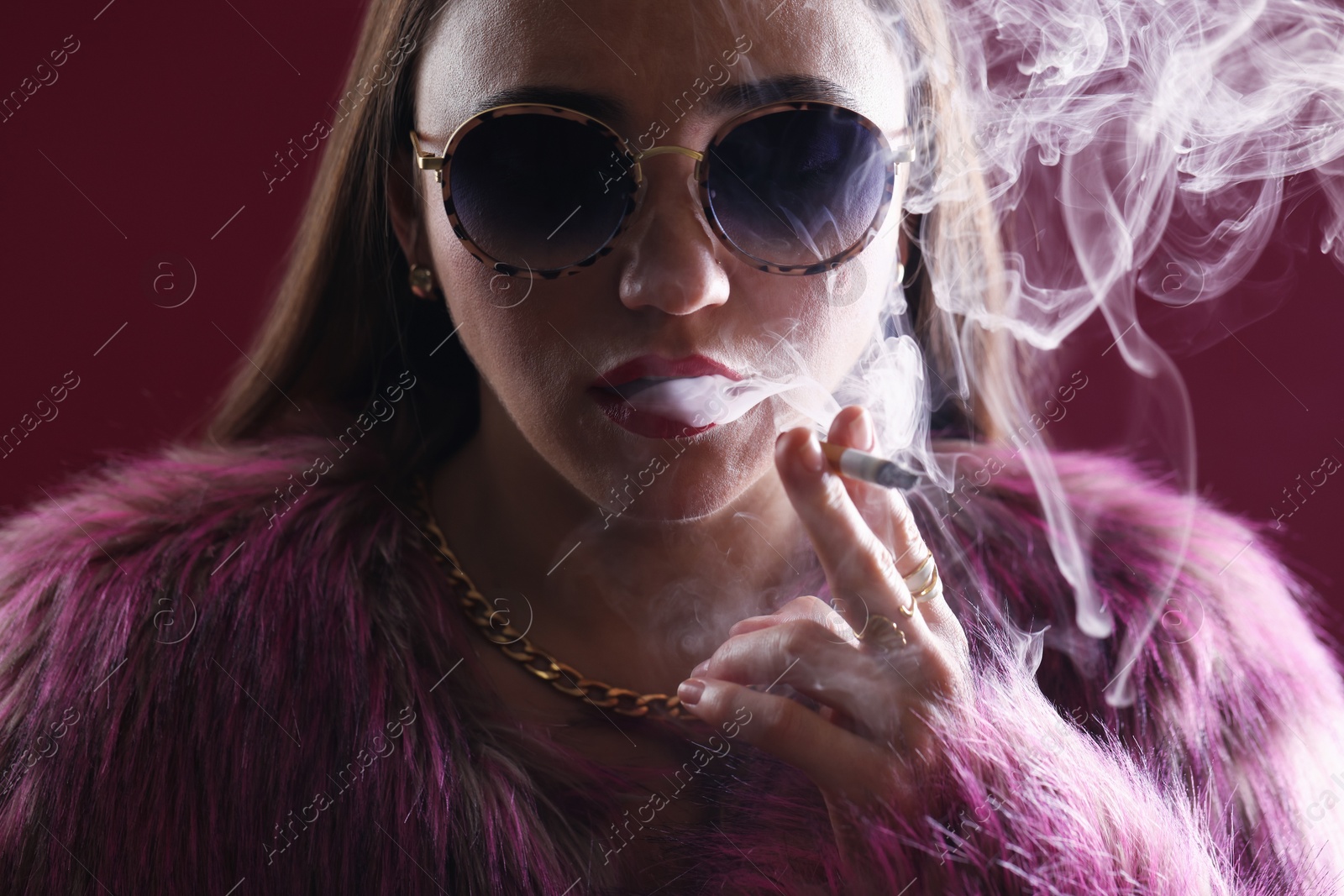 Beautiful woman in fur coat smoking cigarette on dark pink background, closeup Photo of Beautiful woman in fur coat smoking cigarette on dark pink background, closeup