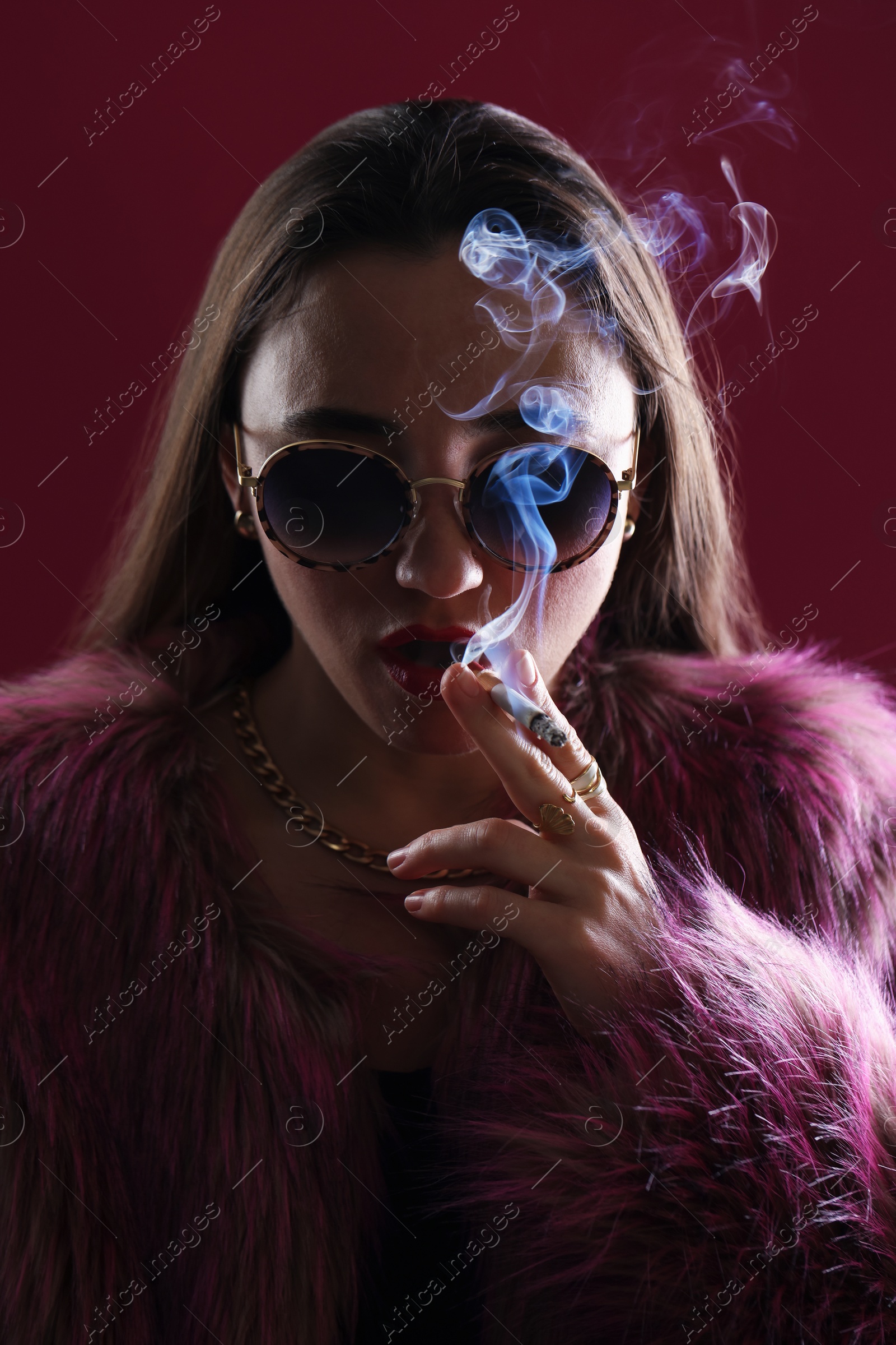 Beautiful woman in fur coat smoking cigarette on dark pink background, closeup Photo of Beautiful woman in fur coat smoking cigarette on dark pink background, closeup