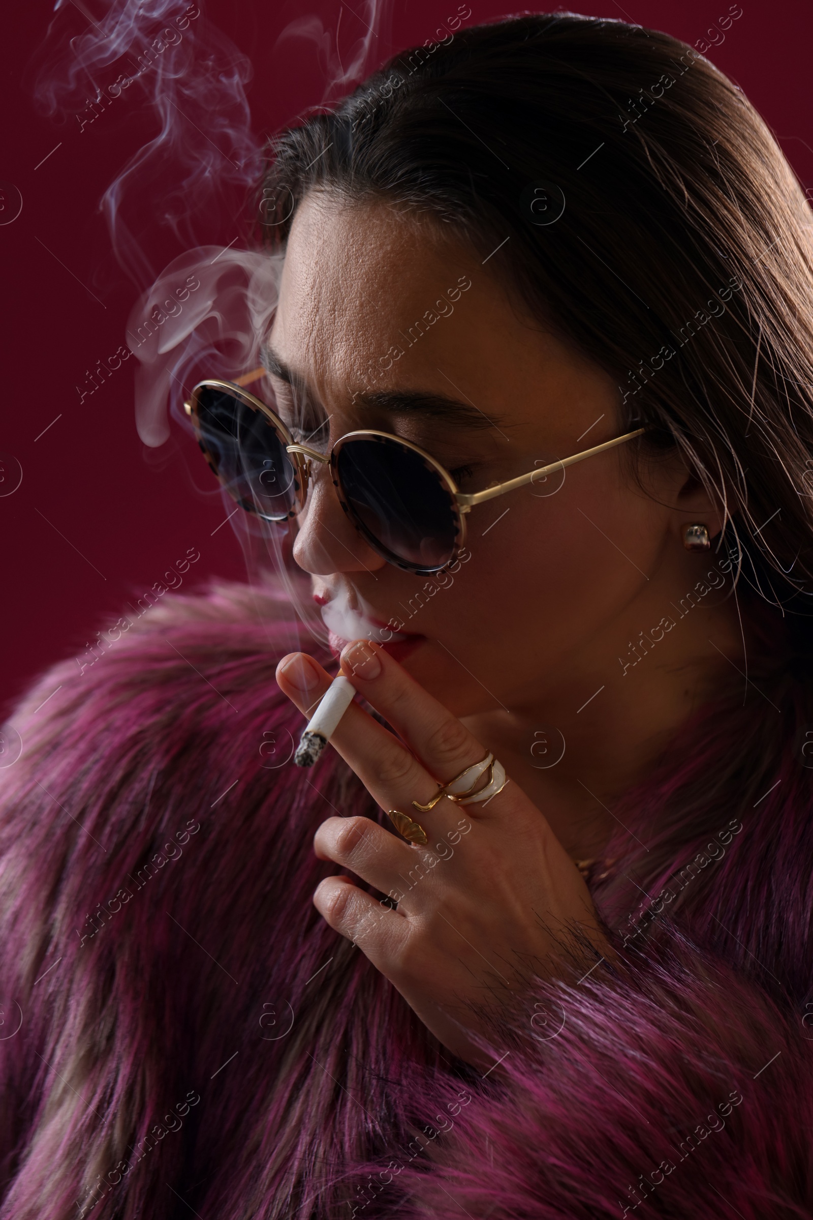 Beautiful woman in fur coat smoking cigarette on dark pink background, closeup Photo of Beautiful woman in fur coat smoking cigarette on dark pink background, closeup