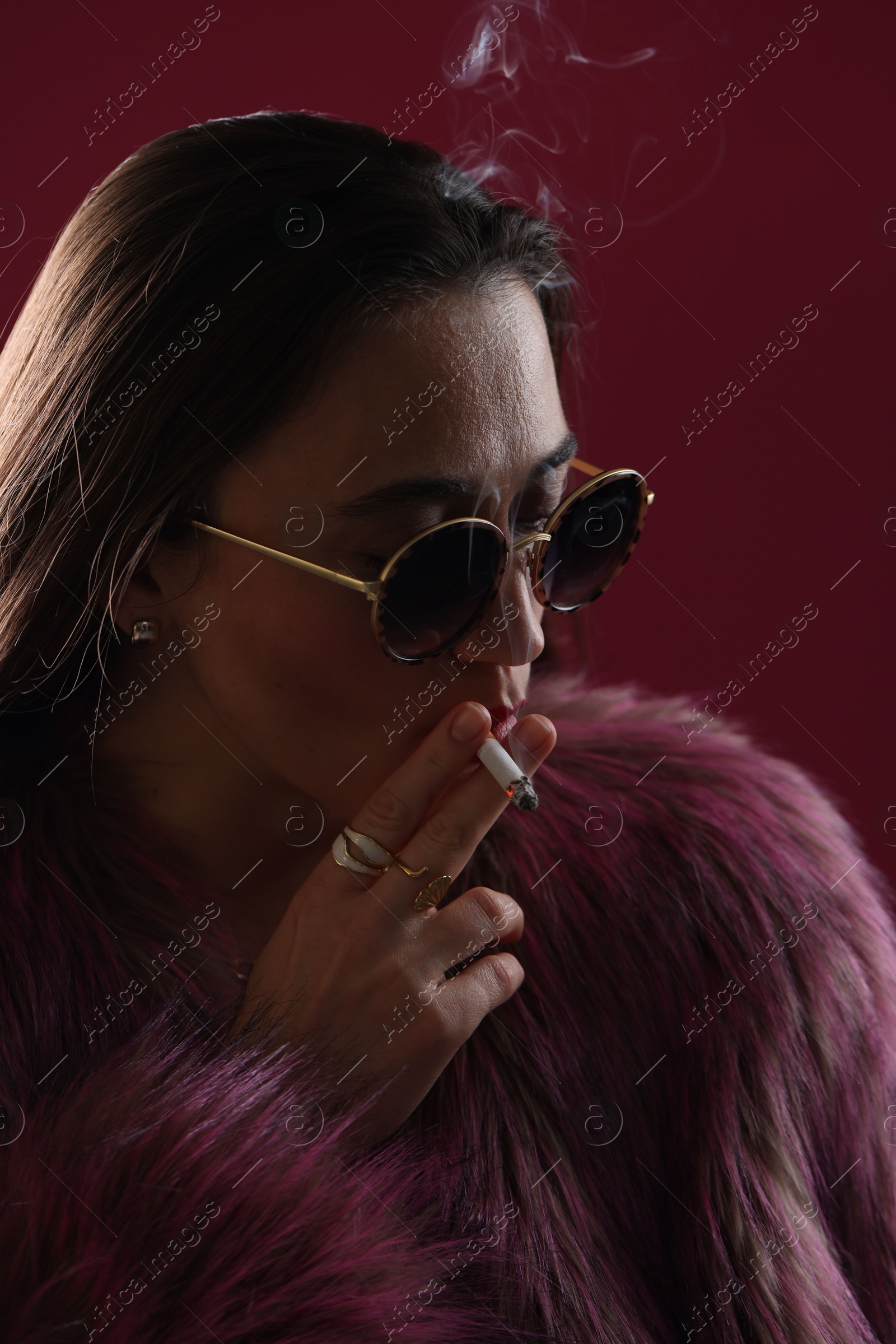 Beautiful woman in fur coat smoking cigarette on dark pink background, closeup Photo of Beautiful woman in fur coat smoking cigarette on dark pink background, closeup