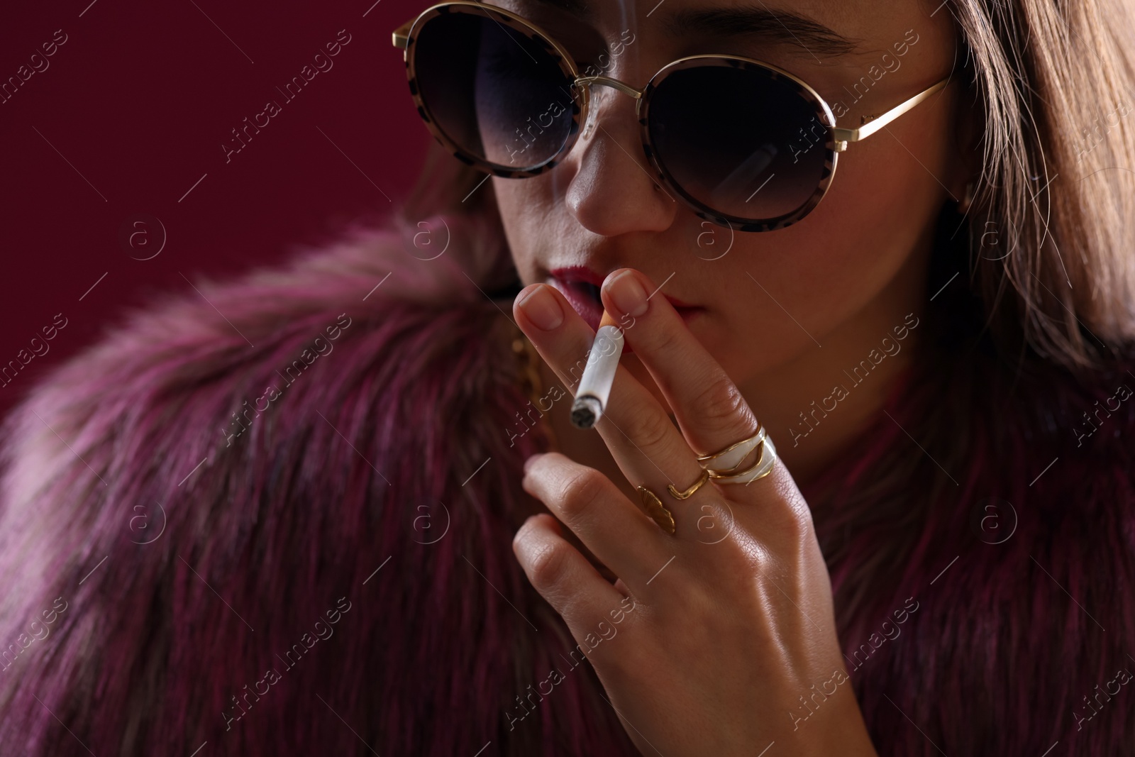 Beautiful woman in fur coat smoking cigarette on dark pink background, closeup Photo of Beautiful woman in fur coat smoking cigarette on dark pink background, closeup