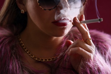 Photo of Beautiful woman smoking cigarette on dark pink background, closeup