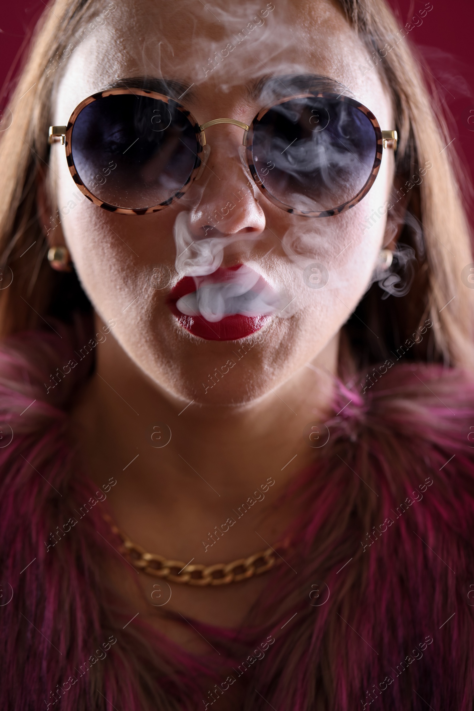 Beautiful woman in fur coat smoking cigarette on dark pink background, closeup Photo of Beautiful woman in fur coat smoking cigarette on dark pink background, closeup