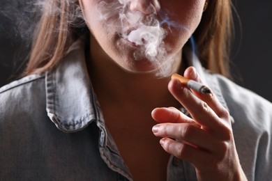 Photo of Woman in shirt smoking cigarette on dark background, closeup. Bad habit