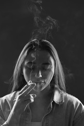 Photo of Woman in shirt smoking cigarette on dark background, black and white effect