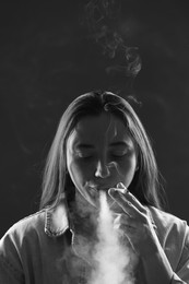 Photo of Woman in shirt smoking cigarette on dark background, black and white effect