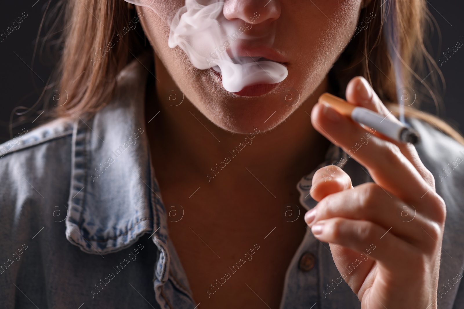 Woman in shirt smoking cigarette on dark background, closeup. Bad habit Photo of Woman in shirt smoking cigarette on dark background, closeup. Bad habit