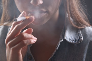 Photo of Woman in shirt smoking cigarette on dark background, closeup. Bad habit