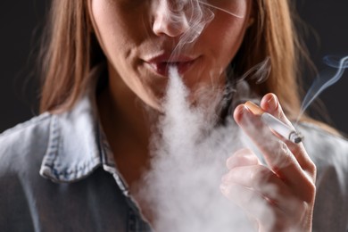 Photo of Woman in shirt smoking cigarette on dark background, closeup. Bad habit