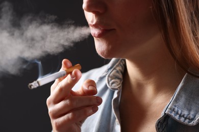 Photo of Woman in shirt smoking cigarette on dark background, closeup. Bad habit