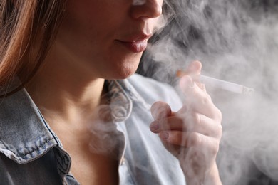Photo of Woman in shirt smoking cigarette on dark background, closeup. Bad habit