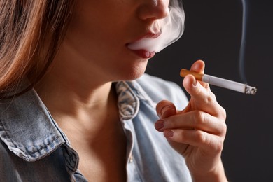 Photo of Woman in shirt smoking cigarette on dark background, closeup. Bad habit