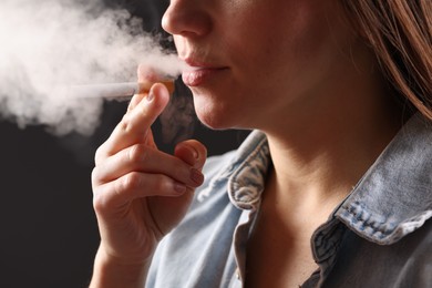 Photo of Woman in shirt smoking cigarette on dark background, closeup. Bad habit