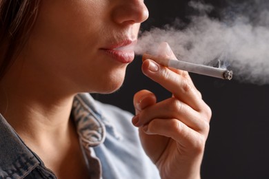 Photo of Woman in shirt smoking cigarette on dark background, closeup. Bad habit