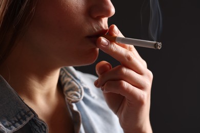 Photo of Woman in shirt smoking cigarette on dark background, closeup. Bad habit