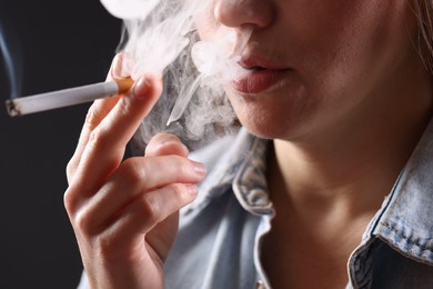 Photo of Woman in shirt smoking cigarette on dark background, closeup. Bad habit