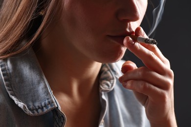 Photo of Woman in shirt smoking cigarette on dark background, closeup. Bad habit