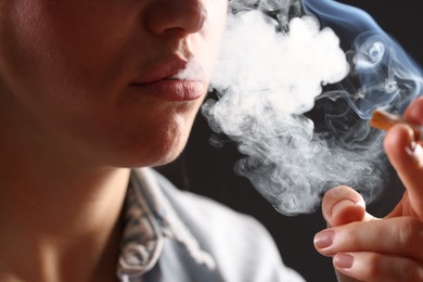Photo of Woman in shirt smoking cigarette on dark background, closeup. Bad habit