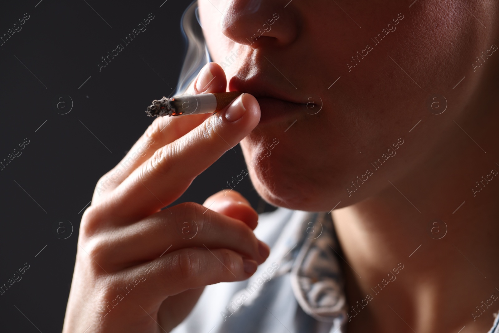 Woman in shirt smoking cigarette on dark background, closeup. Bad habit Photo of Woman in shirt smoking cigarette on dark background, closeup. Bad habit