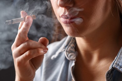 Photo of Woman in shirt smoking cigarette on dark background, closeup. Bad habit