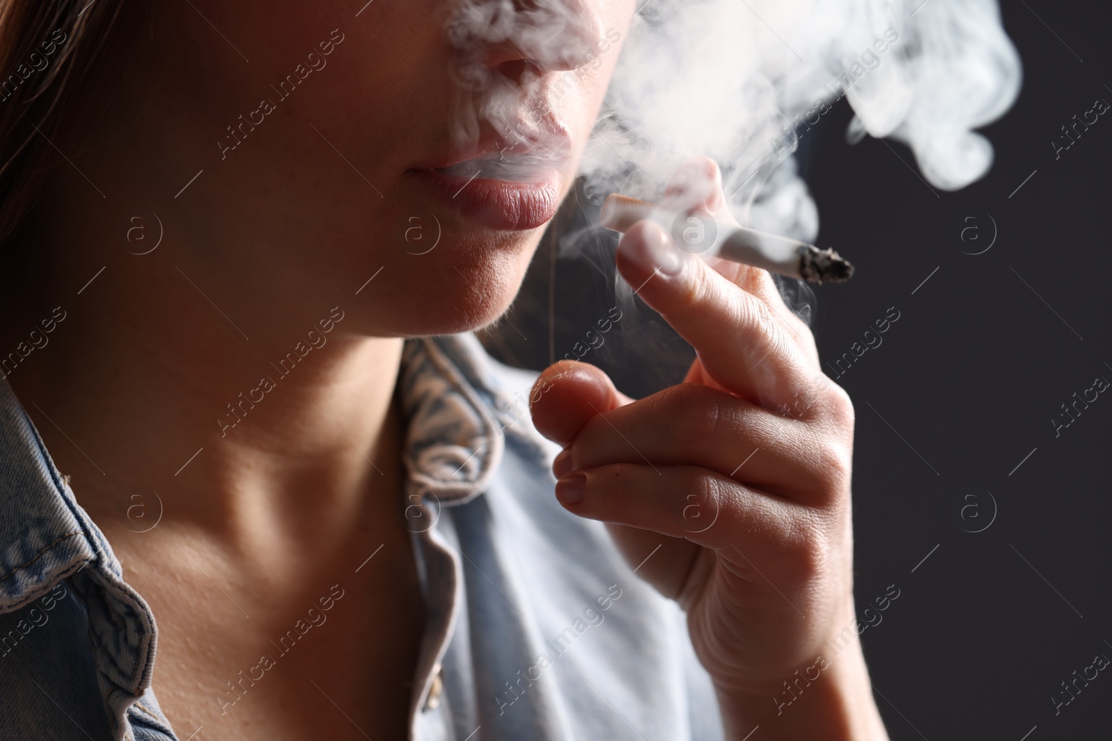 Woman in shirt smoking cigarette on dark background, closeup. Bad habit Photo of Woman in shirt smoking cigarette on dark background, closeup. Bad habit