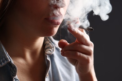 Photo of Woman in shirt smoking cigarette on dark background, closeup. Bad habit