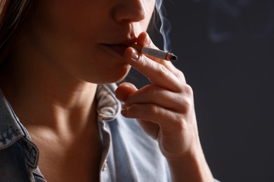 Photo of Woman in shirt smoking cigarette on dark background, closeup. Bad habit
