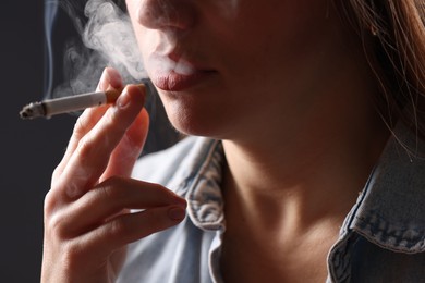 Photo of Woman in shirt smoking cigarette on dark background, closeup. Bad habit
