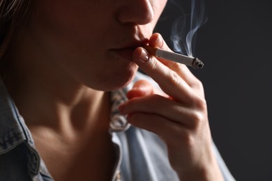 Photo of Woman in shirt smoking cigarette on dark background, closeup. Bad habit