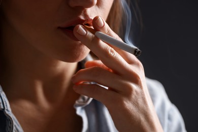 Photo of Woman in shirt smoking cigarette on dark background, closeup. Bad habit