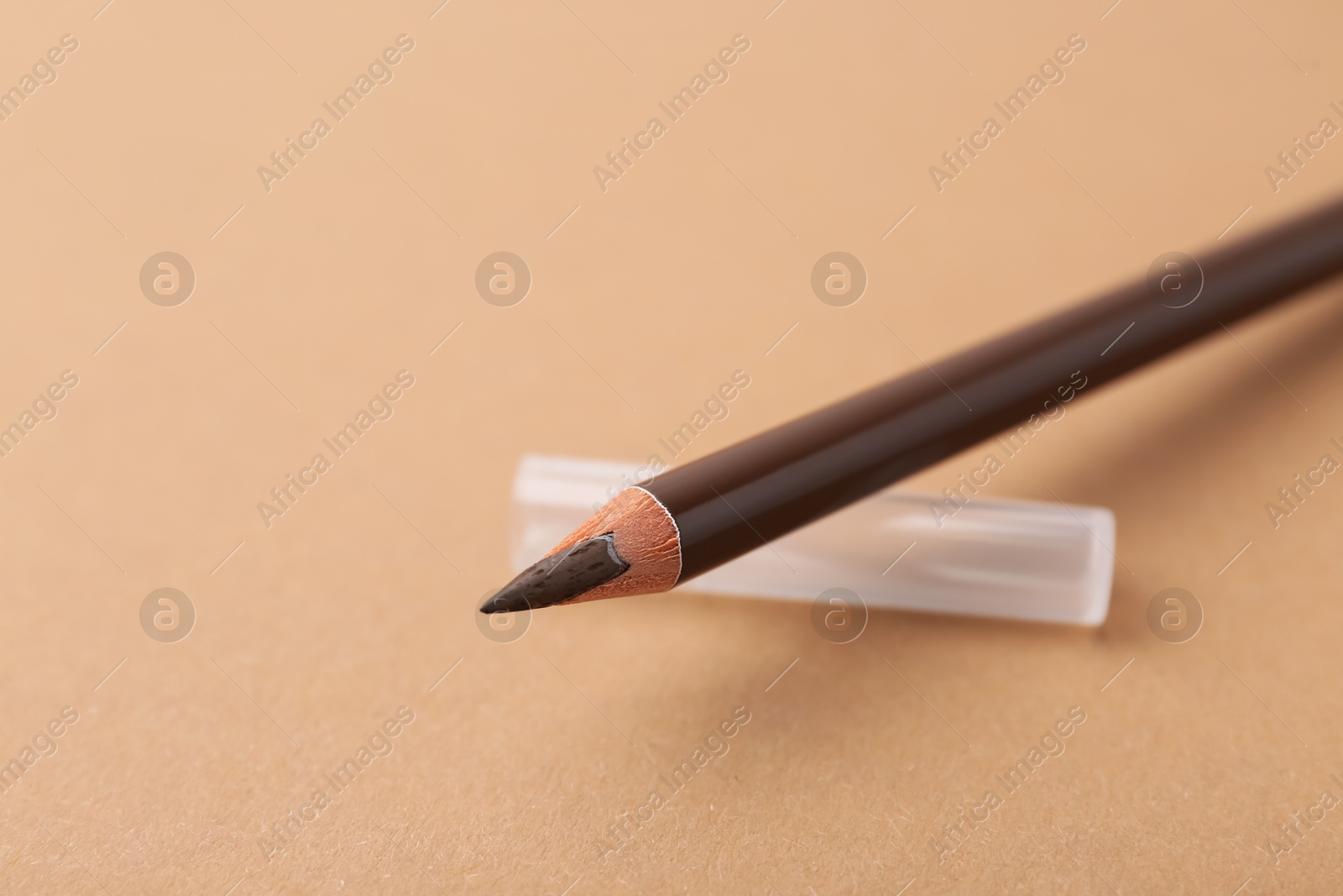 Photo of Brown eyebrow pencil on beige background, closeup. Space for text