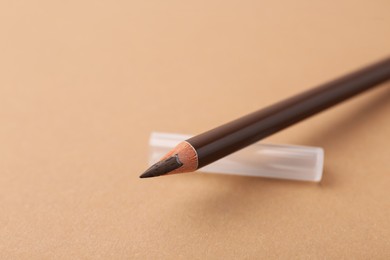 Photo of Brown eyebrow pencil on beige background, closeup. Space for text