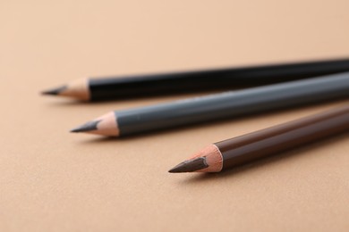 Photo of Three different eyebrow pencils on beige background, closeup
