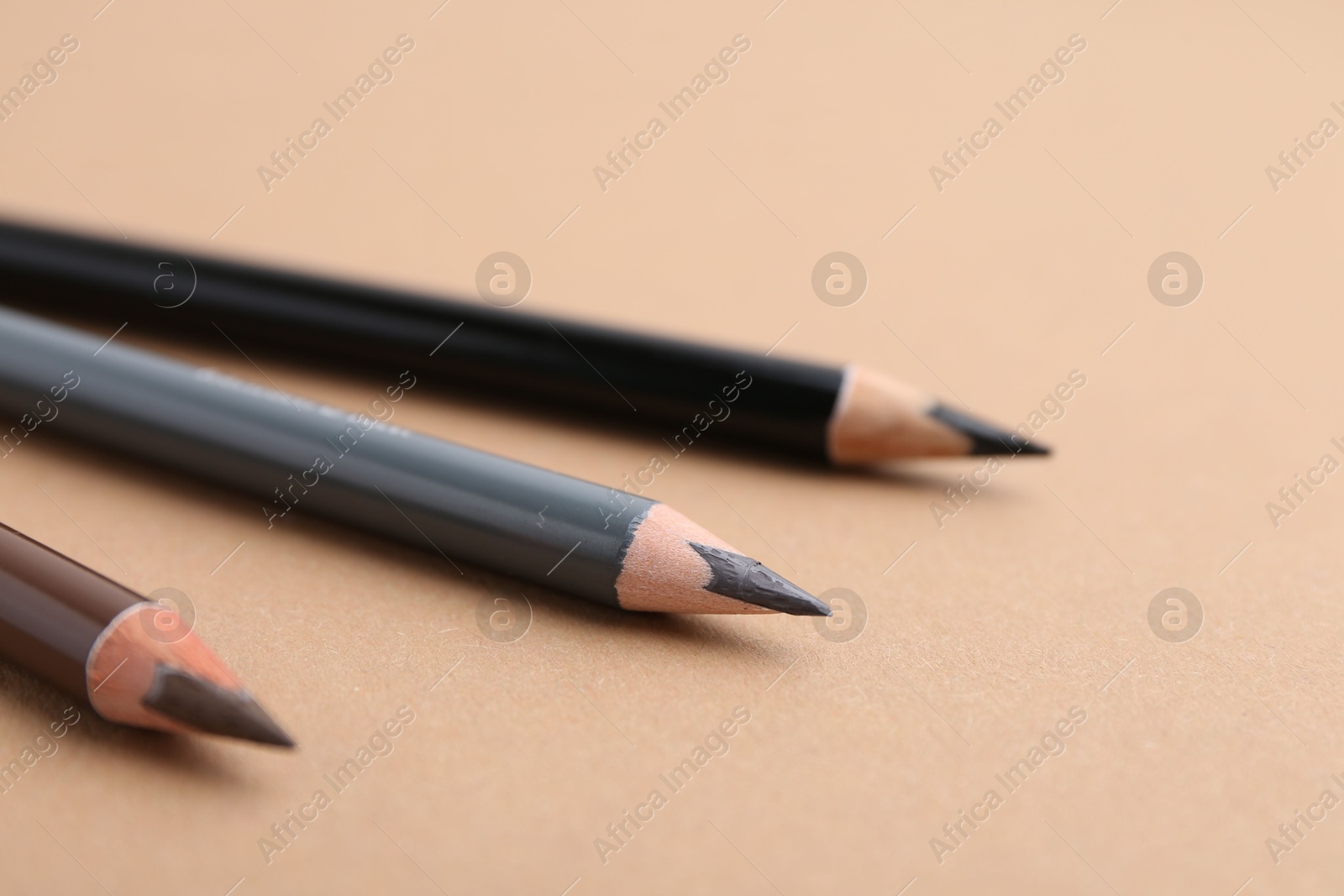 Three different eyebrow pencils on beige background, closeup Photo of Three different eyebrow pencils on beige background, closeup
