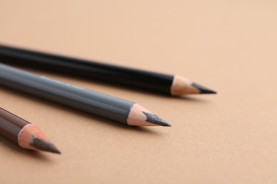 Photo of Three different eyebrow pencils on beige background, closeup