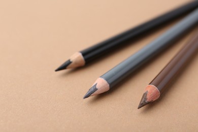 Photo of Three different eyebrow pencils on beige background, closeup. Space for text