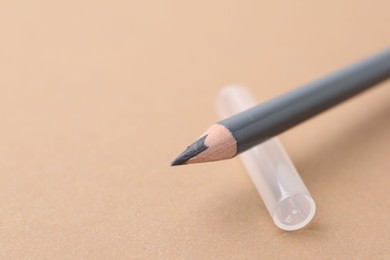 Photo of Grey eyebrow pencil on beige background, closeup. Space for text