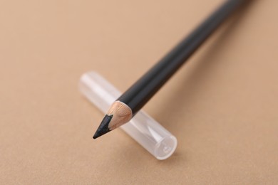 Photo of Black eyebrow pencil on beige background, closeup