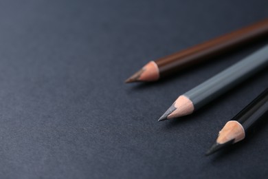 Photo of Three different eyebrow pencils on dark background, closeup. Space for text