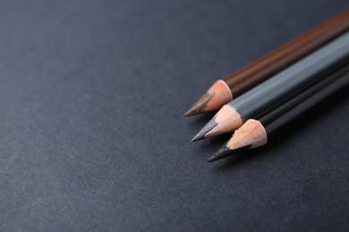 Photo of Three different eyebrow pencils on dark background, closeup. Space for text