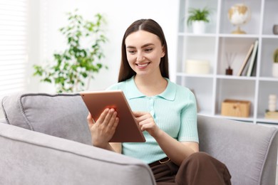 Photo of Young woman using modern tablet in armchair at home